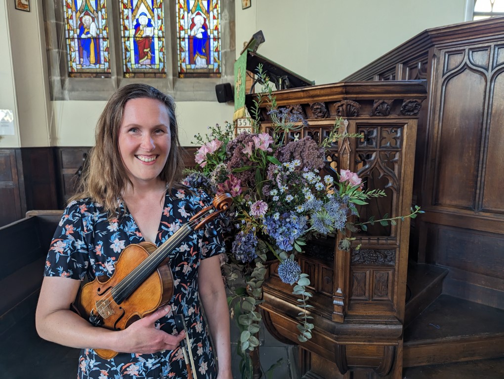 Violinist Zoe Beyers standing in front of a font and some flowers in St Alkmund's Church Shrewsbury