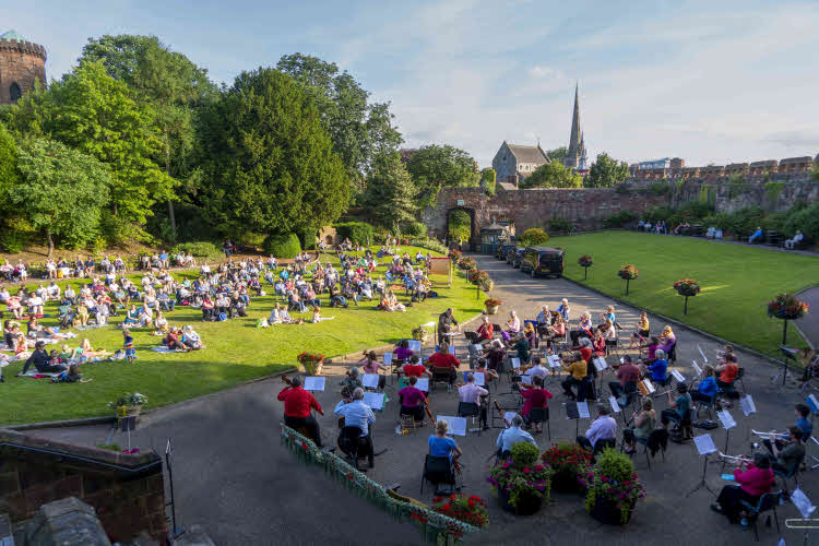 A view from the steps to the castle overlooking the orchestra and beyond them the audience on the grass