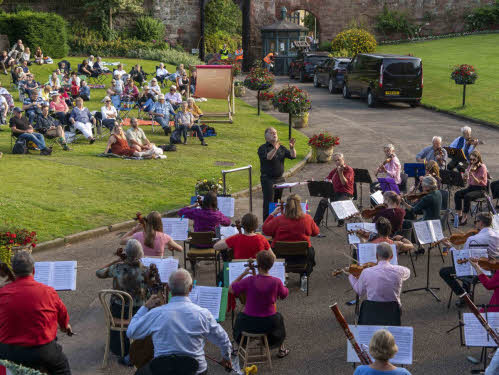 A photo of John Moore conducting the orchestra at the July 2021 concert in Shrewsbury Castle with the audience in the background [pic Andy Bell]